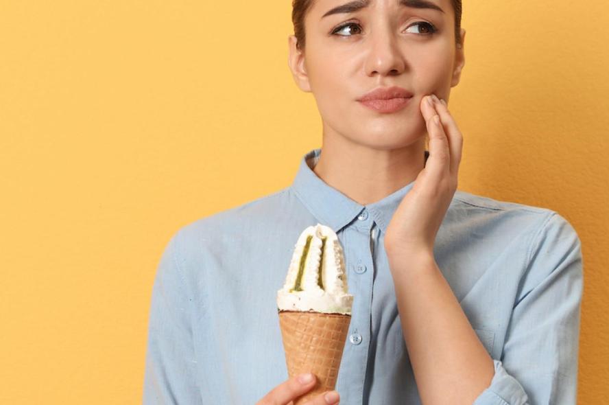 A woman holding an ice cream cone and clutching her cheek in pain
