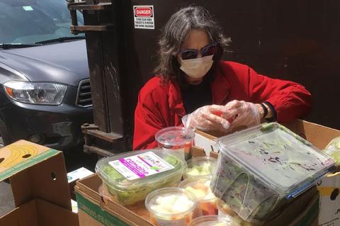 A woman wearing a protective mask sorts packaged fruits and vegetables in a parking lot. Tufts University is donating the use of one of its dining centers to a coalition of Massachusetts food rescue organizations during the pandemic.