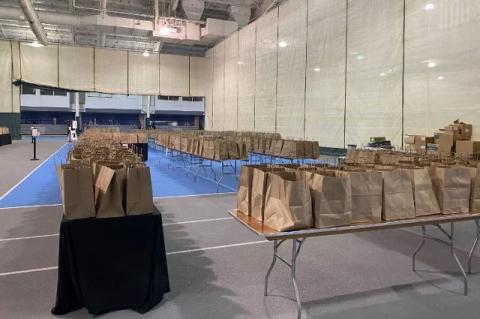 Rows of paper bags on tables in a gymnasium. Tufts organized meals for students staying on campus over Thanksgiving, with help from local restaurants