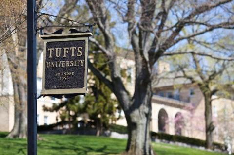 A Tufts sign with campus buildings in the background