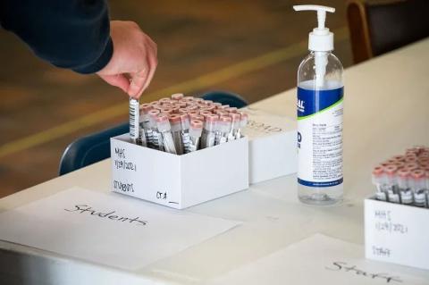 A hand puts a container with testing swabs into a box containing other swabs