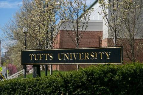 A photo of a Tufts University sign with trees blooming behind it