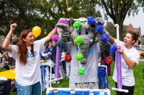 The Jumbo mascot runs through the “car wash” as two Tufts volunteers cheer on the Academic Quad at Tufts University for Community Day 2023