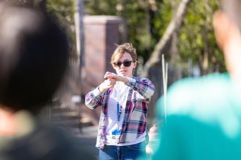 A young woman standing outdoors with her hands clasped in front of her, as two students look on. An after-school program run by undergraduates at Hillel brings Medford youngsters to Tufts’ campus
