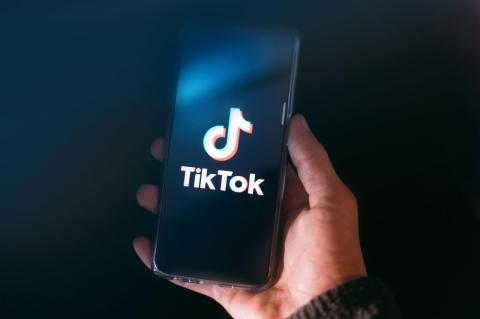 A persona’s hand holding a smartphone with the screen showing Tiktok’s logo. An expert on attention says TikTok has some advantages over other social media that keep it addictive, but that the real fear seems geopolitical.  