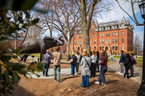 Students and parents stand around a statue of Jumbo the elephant listening to a Tufts tour guide. 