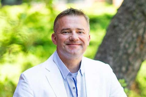 A photo of a man in a white jacket sitting on a wooden bench