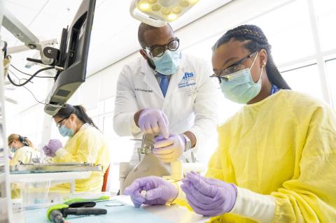 A dental professor consults with a high school student who holds a mock tooth in the dental simulation clinic,