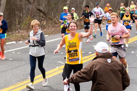 Naomi Arnold, E26, waving and running up to Tufts Marathon Team Coach Don Megerle at mile nine on the Boston Marathon route