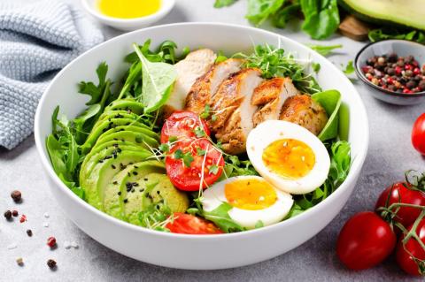 A bowl of salad with grilled chicken, hard-boiled eggs, and sliced avocado.